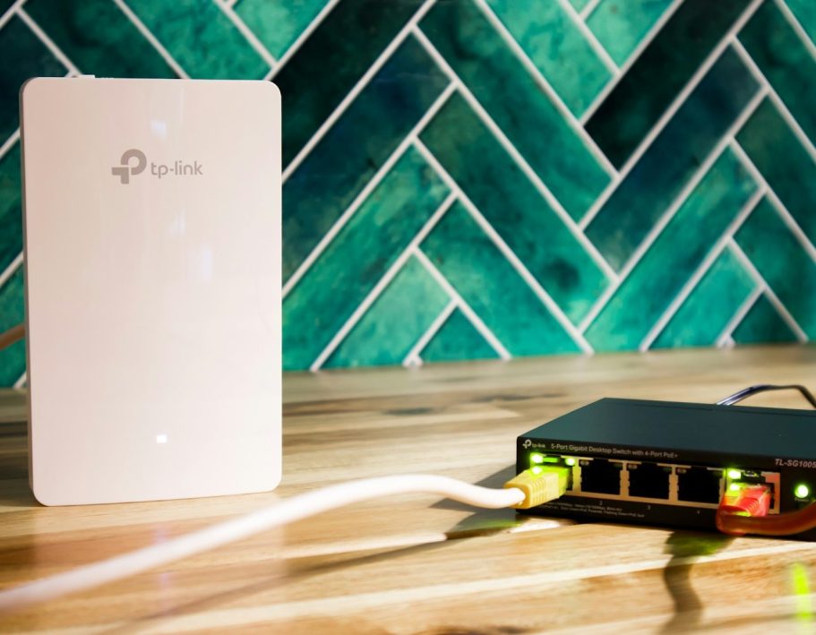 Ein Netzwerkgerät und ein Router auf einer Holzoberfläche vor grünem Fliesenmuster.
